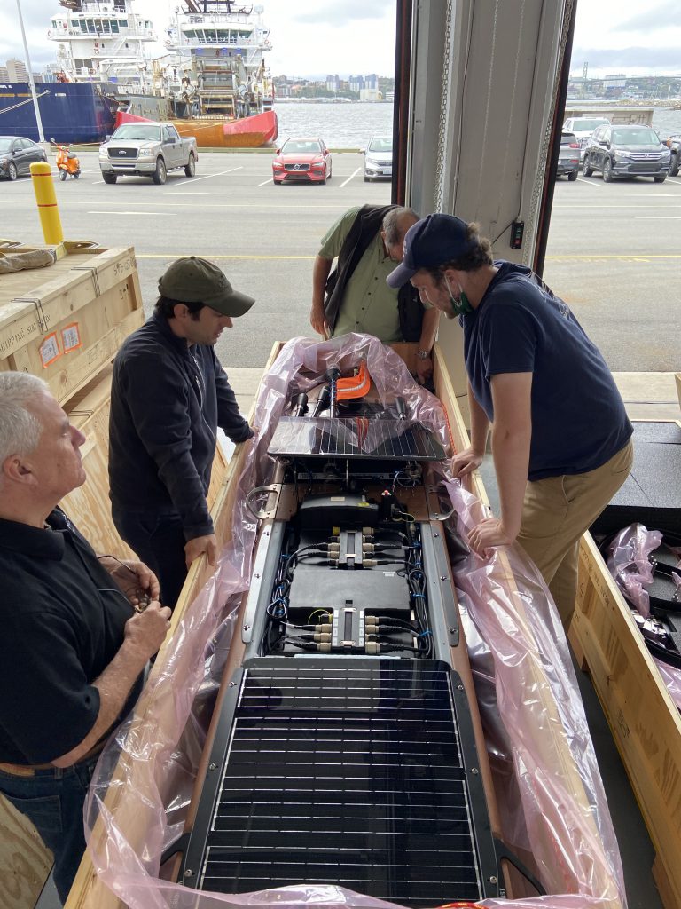 A group of men stand over a wave glider in a garage